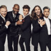 Five stars of Queer Eye stand together in matching black suits, posing for the camera, smiling