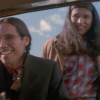 Still from Smoke Signals featuring Evan Adams with long braided hair and glasses and Adam Beach with long hair, both looking into a car window