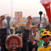 A crowd of fans watch the World Cup in South Africa: a woman raised her hands in victory at the foreground of the image with fans dressed in soccer gear behind