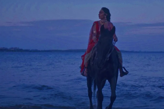 Woman in red sits atop a horse riding out of the blue ocean
